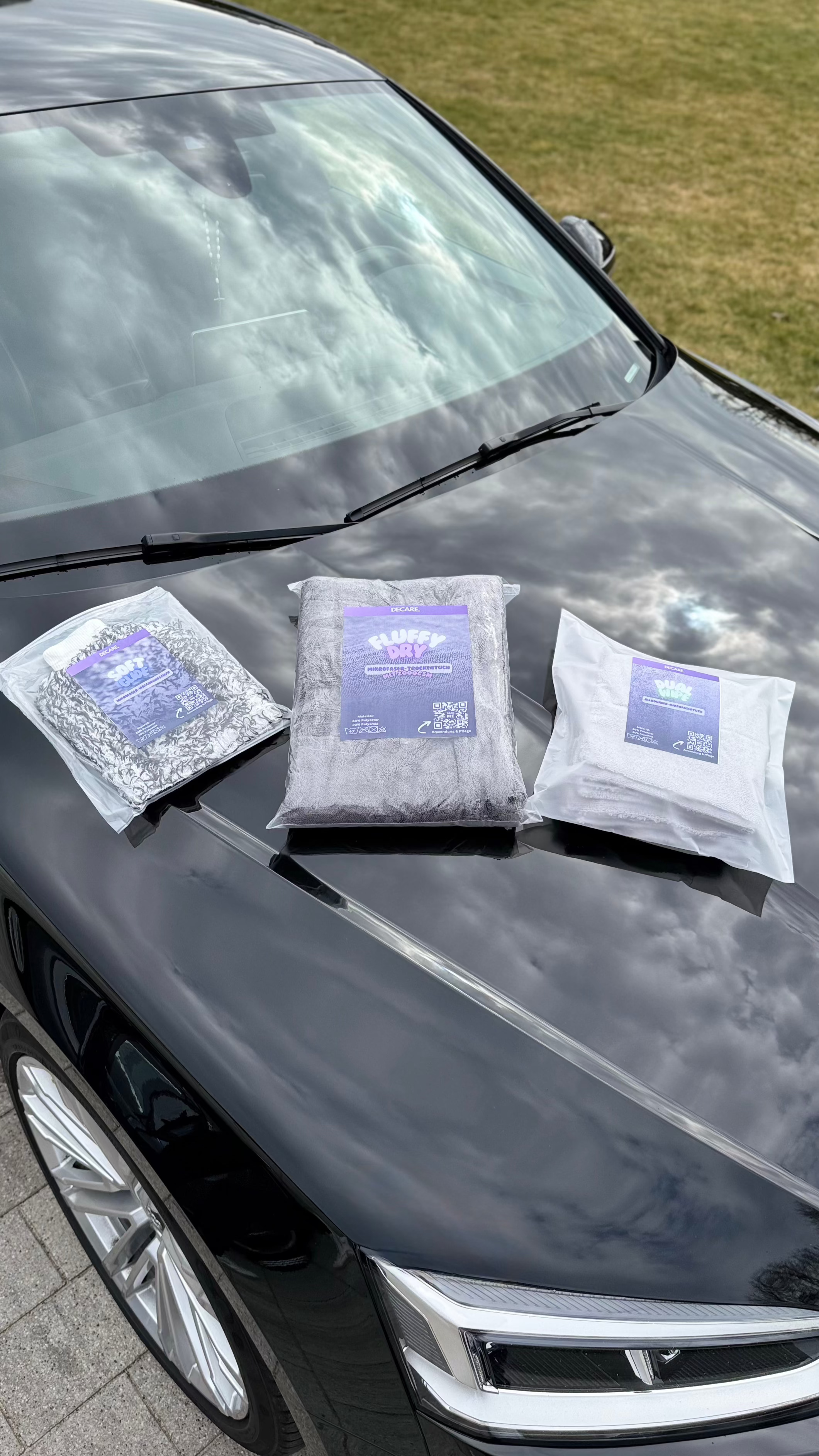 Die drei Decare Autopflegeprodukte SoftGlide, FluffyDry und DualWipe in Verpackung auf einer Motorhaube – Bannerbild für hochwertigen Fahrzeugglanz